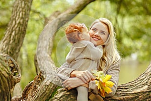 Mum gently embraces the redhead baby girl on autumn forest background