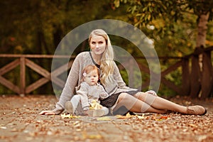 Mum gently embraces the redhead baby girl on autumn forest background