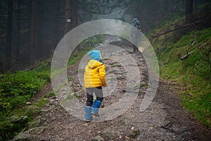 Mum and her little son go on a mountain trail in wet autumn weather. They are accompanied by a dog