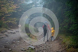 Mum and her little son go on a mountain trail in wet autumn weather. They are accompanied by a dog