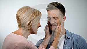 Mum pinching adult son cheeks, male smiling, overprotection effect concept