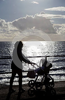 Mum with pram walking along sea front silhouettte