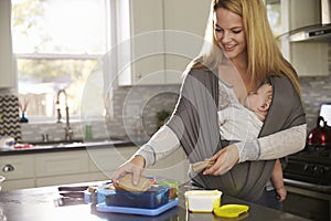 Mum preparing lunchbox while baby sleeps on her in a carrier