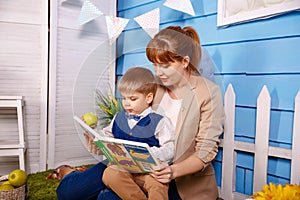 Mum reading fairy tale book to child son sitting on floor. Babysitter