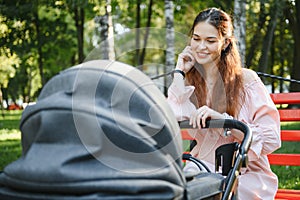 Mum sitting on a bench. Woman pushing her toddler sitting in a pram. Family concept