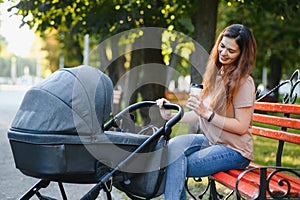 Mum sitting on a bench. Woman pushing her toddler sitting in a pram. Family concept