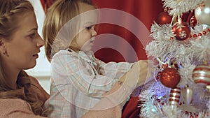 Mum with a small daughter decorate a Christmas tree