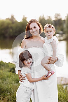 Mum with two little daughters outdoors on summer. Young mother with baby girls walk on beach near lake. Family holiday