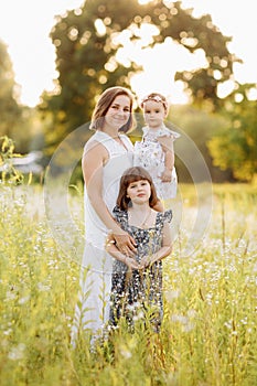 Mum with two little daughters outdoors on summer. Young mother with baby girls walk on beach near lake. Family holiday