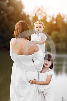 Mum with two little daughters outdoors on summer. Young mother with baby girls walk near lake. Family holiday on pond