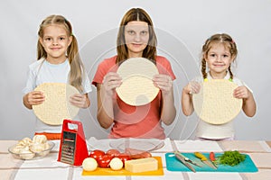 Mum with two little girls sitting in a row at kitchen table and a hand-held pizza bases