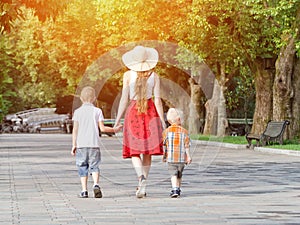 Mum and two sons walking in the park, sunny day. View from the back