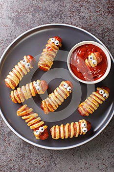 Mummy sausage in dough scary Halloween holiday food with funny eyes and sauce on a plate. vertical top view