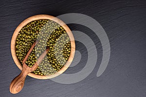 Mung bean in a wooden cup and wooden scoop on a black stone board background, space for text, beans