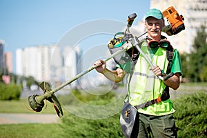 Municipal gardener landscaper worker with gas grass string trimmer photo