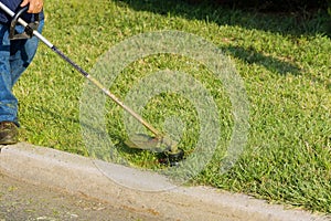 A municipal worker with a lawn mower mows fresh green grass near a road using a hand lawn mower