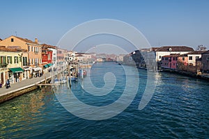 Murano, Italy day view of the main canal with low-rise colorful buildings and moored boats on wooden wharf pilings