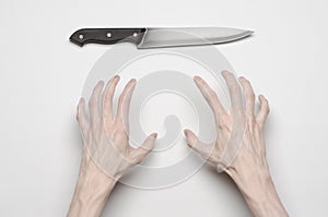 Murder and Halloween theme: A man's hand reaching for a knife, a human hand holding a knife isolated on a gray background in