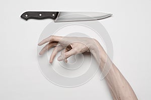 Murder and Halloween theme: A man's hand reaching for a knife, a human hand holding a knife isolated on a gray background in