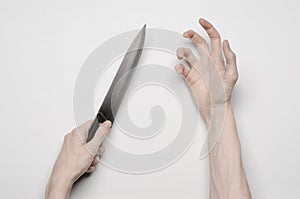 Murder and Halloween theme: A man's hand reaching for a knife, a human hand holding a knife isolated on a gray background in