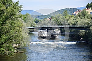 Mursteg footbridge over the River Mura, the futuristic Island in the Mur with frame of trees, hills and sky in Graz.