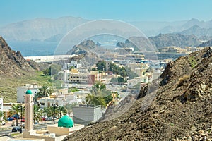 Muscat Takia historical city center streets overview panorama with green mosque some, rocks and arabian sea in the background,