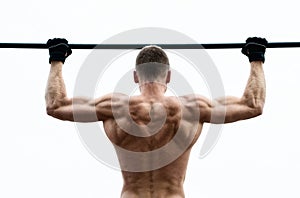 Muscle man making pull-up on horizontal bar against the sky