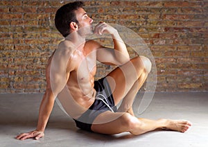 Muscle shaped man sitting relaxed on brickwall