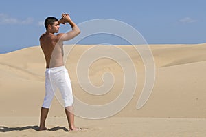 Muscled man in the desert dunes with white trouser