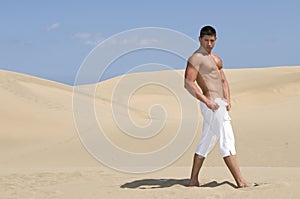 Muscled man in the desert dunes with white trousse photo