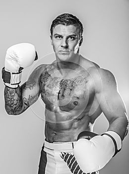 A muscled man with many tattoos wearing white boxing gloves