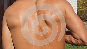 Muscles of the back of a sexy, sunburnt pumped up young worker. Sweat on back, bare torso