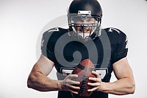 Muscular american football player in protective uniform and helmet holding ball