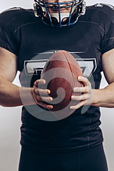 Muscular american football player in protective uniform and helmet holding ball