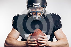 Muscular american football player in protective uniform and helmet holding ball