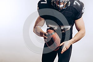 Muscular american football player in protective uniform and helmet holding ball