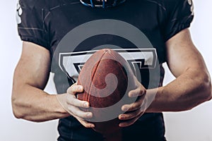 Muscular american football player in protective uniform and helmet holding ball