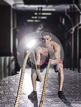 Muscular athlete with battle rope battle ropes exercise in the f