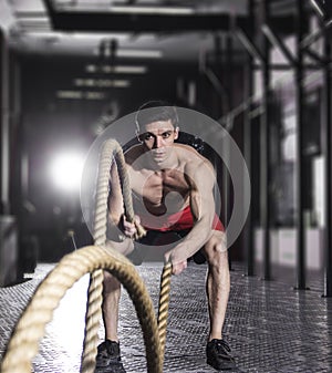 Muscular athlete with battle rope battle ropes exercise in the f
