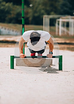 Muscular athlete exercising push up outside in sunny park