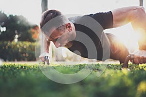 Muscular athlete exercising push up outside in sunny park. Fit shirtless male fitness model in crossfit exercise photo