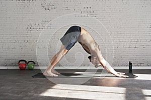 Muscular athlete exercising yoga asana in sunny sport club, brick wall. Fit shirtless male fitness model.