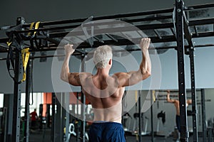 Muscular athlete man making Pull-up in gym. Bodybuilder training in fitness club showing his perfect back and shoulder