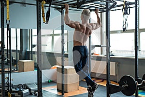 Muscular athlete man making Pull-up in gym. Bodybuilder training in fitness club showing his perfect back and shoulder