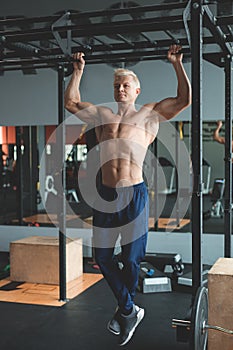 Muscular athlete man making Pull-up in gym. Bodybuilder training in fitness club showing his perfect back and shoulder