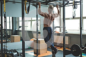 Muscular athlete man making Pull-up in gym. Bodybuilder training in fitness club showing his perfect back and shoulder