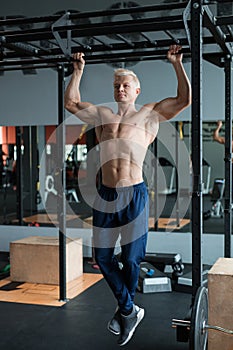 Muscular athlete man making Pull-up in gym. Bodybuilder training in fitness club showing his perfect muscles.