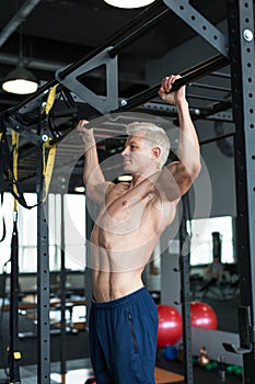 Muscular athlete man making Pull-up in gym. Bodybuilder training in fitness club showing his perfect muscles.