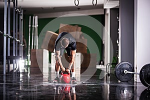 Muscular athlete power lifting a kettlebell. Man working out indoors