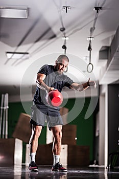 Muscular athlete power lifting a kettlebell. Man working out indoors